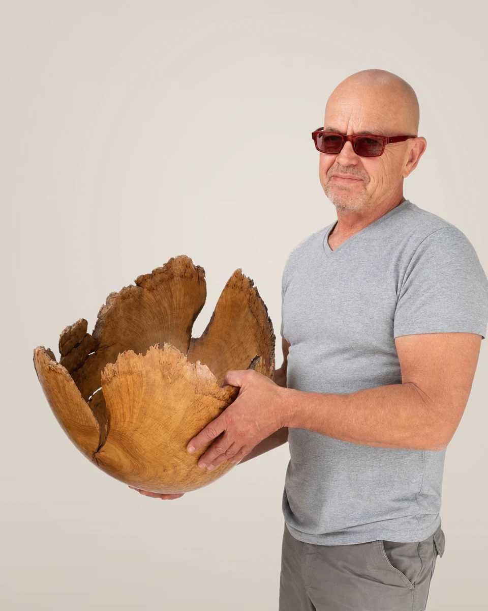 Rodney Band standing with a sculptural wooden bowl against a softly graduated warm-stone studio backdrop.