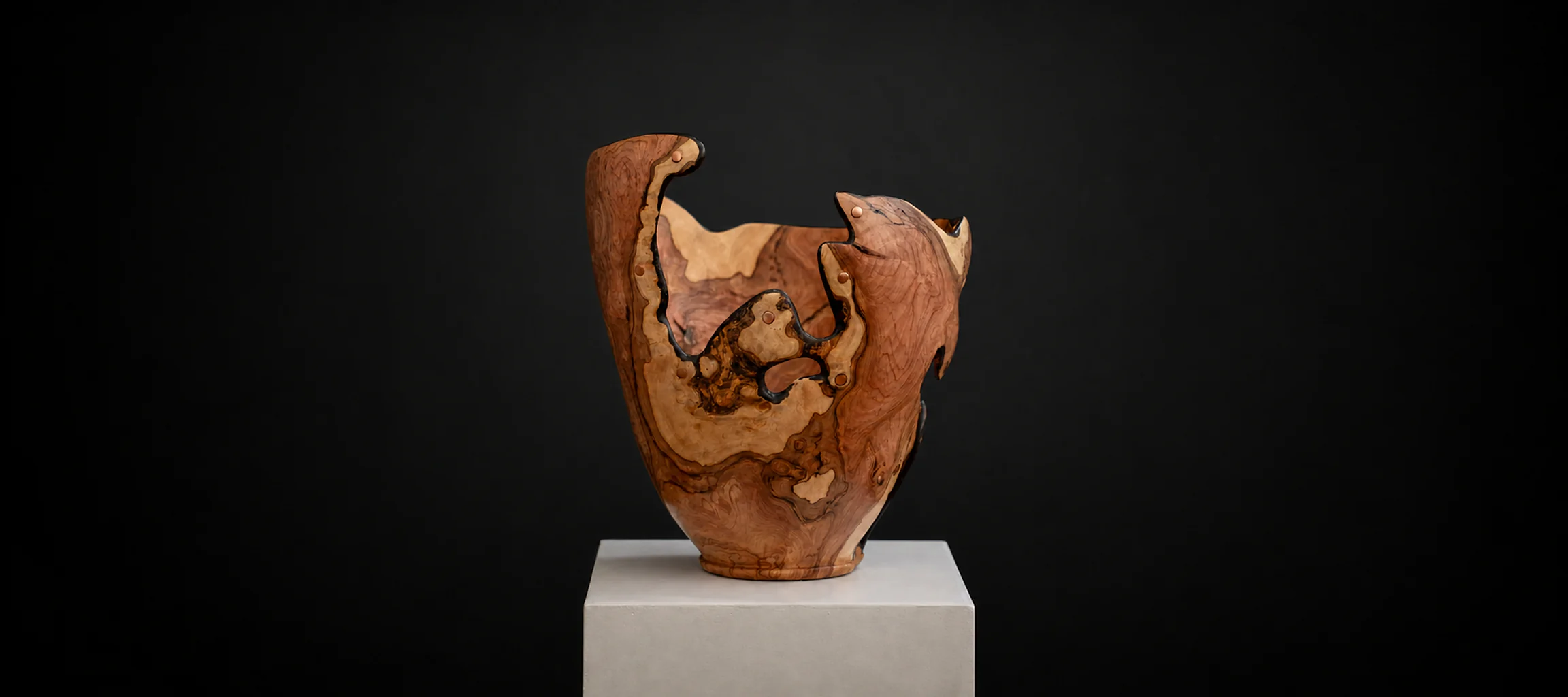 Tall Sculptural Wild Olive Bowl, a one-of-one Wild Olive sculpture by Rodney Band, centred on a warm limestone plinth against a charcoal studio ground.