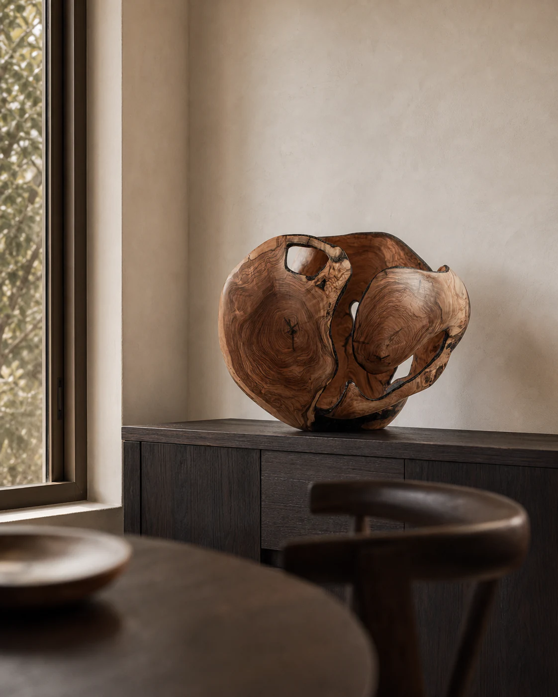 One-of-one olive and blackwood sculpture placed on a dark oak credenza in a quiet interior.