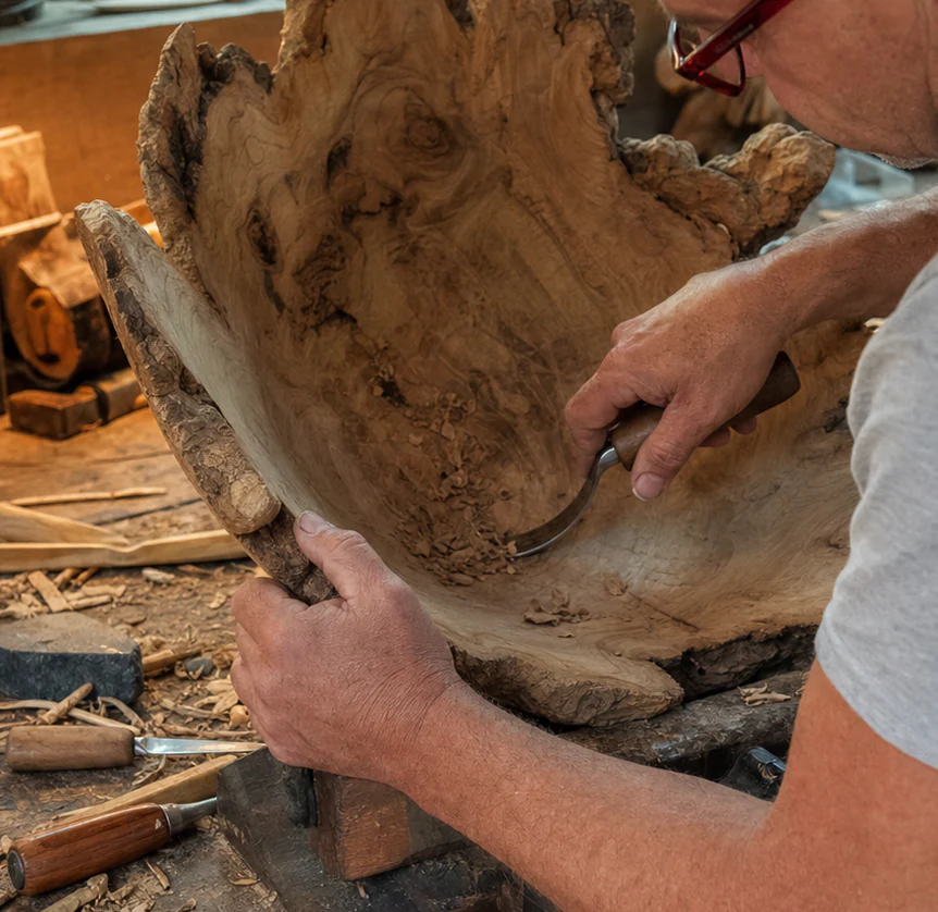 Rodney hand-carving the interior of an unfinished root bowl at his workbench.