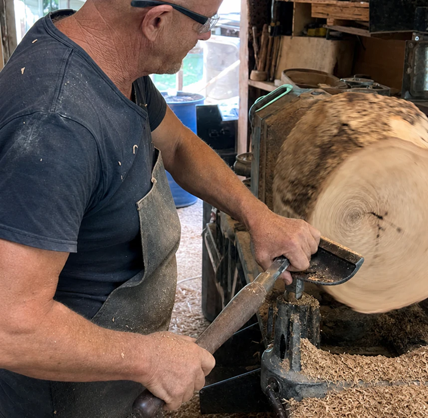 Rodney Band shaping a rough Wild Olive log on his workshop lathe.