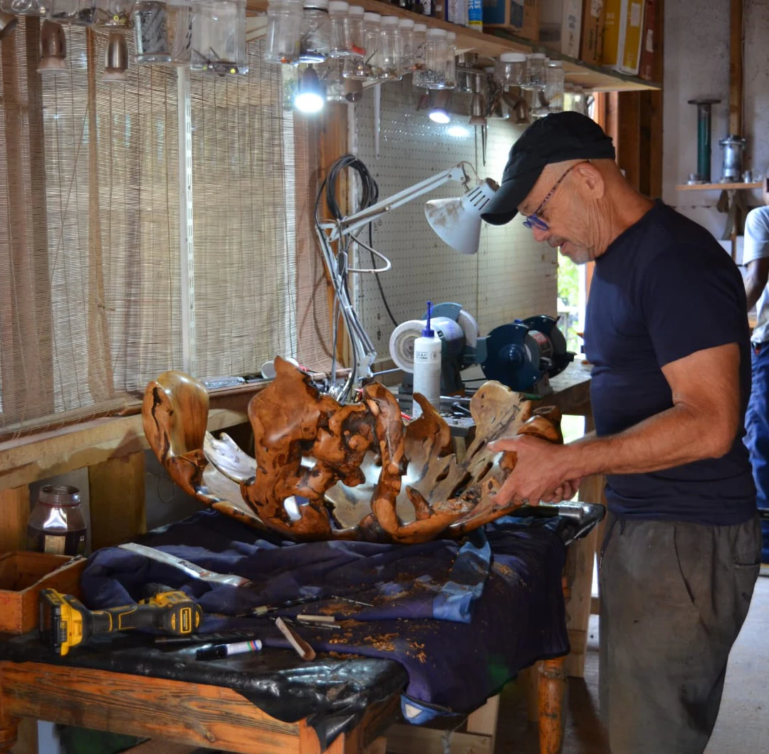 Rodney Band handling an intricate wooden sculpture at his studio workbench.